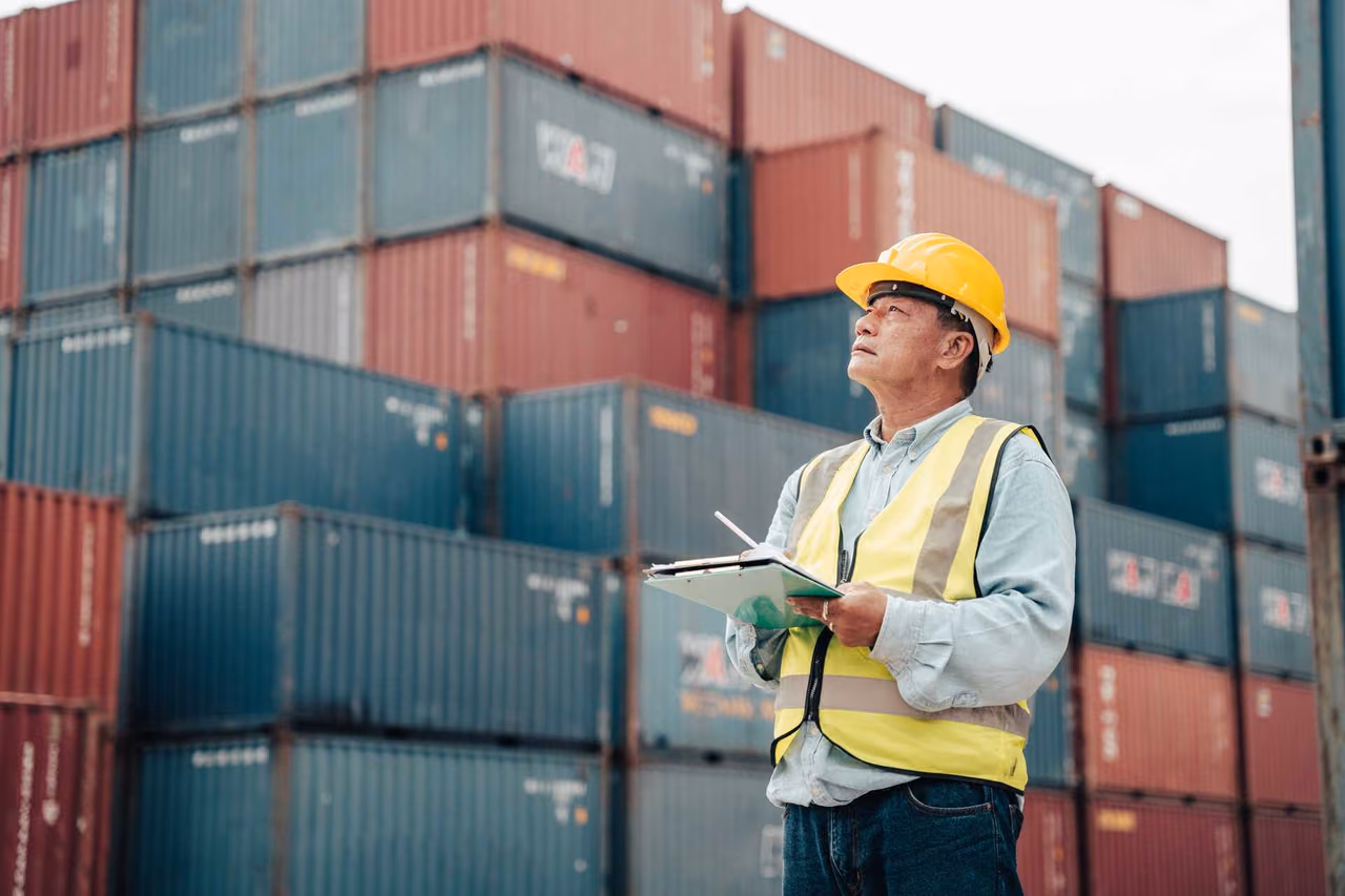 Inspector with helmet and clipboard between containers