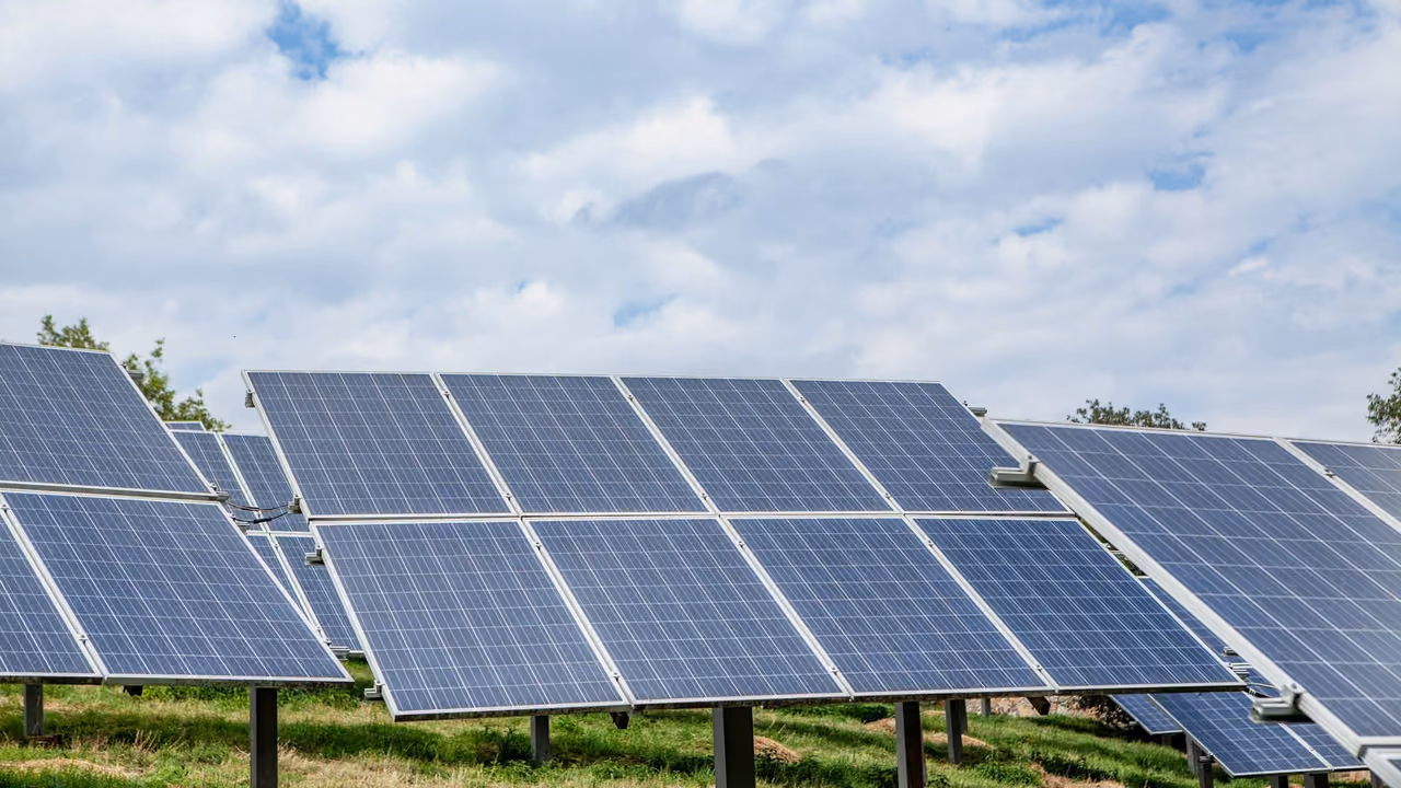 Ground-mounted solar panels in a meadow under a cloudy sky
