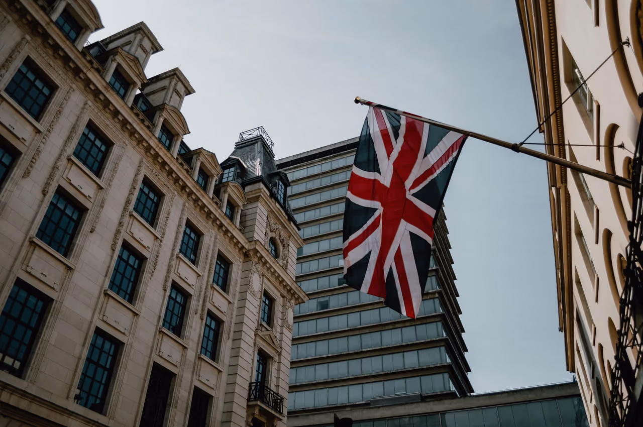 Union flag on a flagpole between a stone facade and an office tower on a London street
