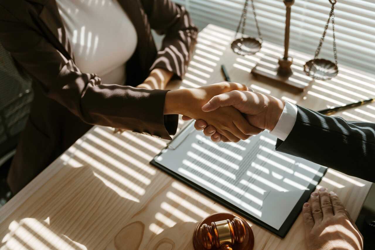 Two people shaking hands over a desk with scales of justice