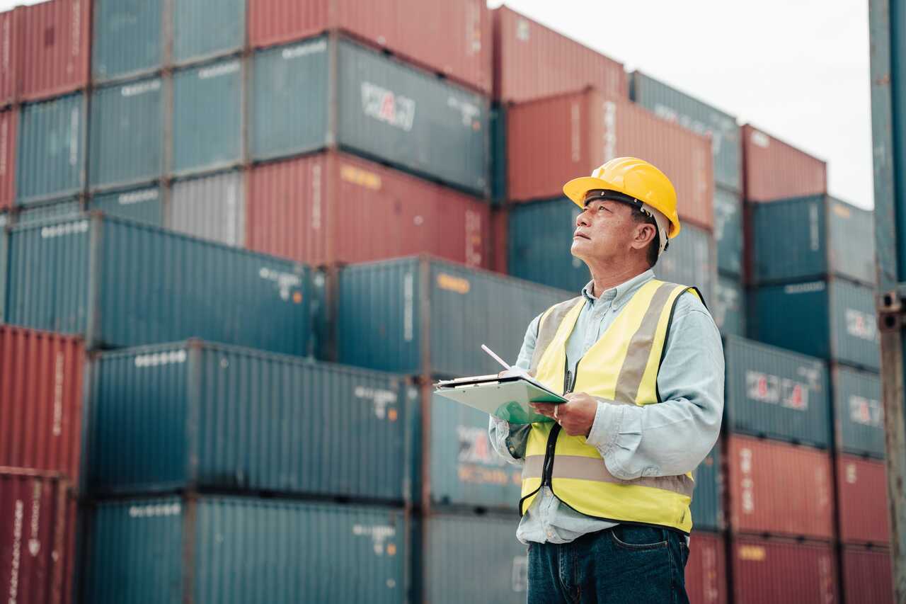 Inspector with hard hat and clipboard between shipping containers